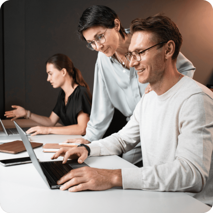 A person is using his computer in an office setting with coworkers nearby.