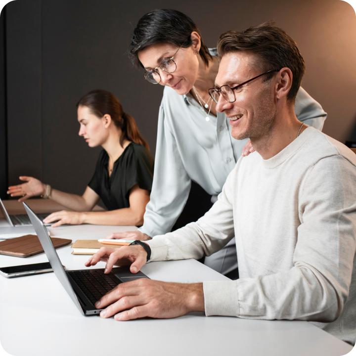 A person is using his computer in an office setting with coworkers nearby.